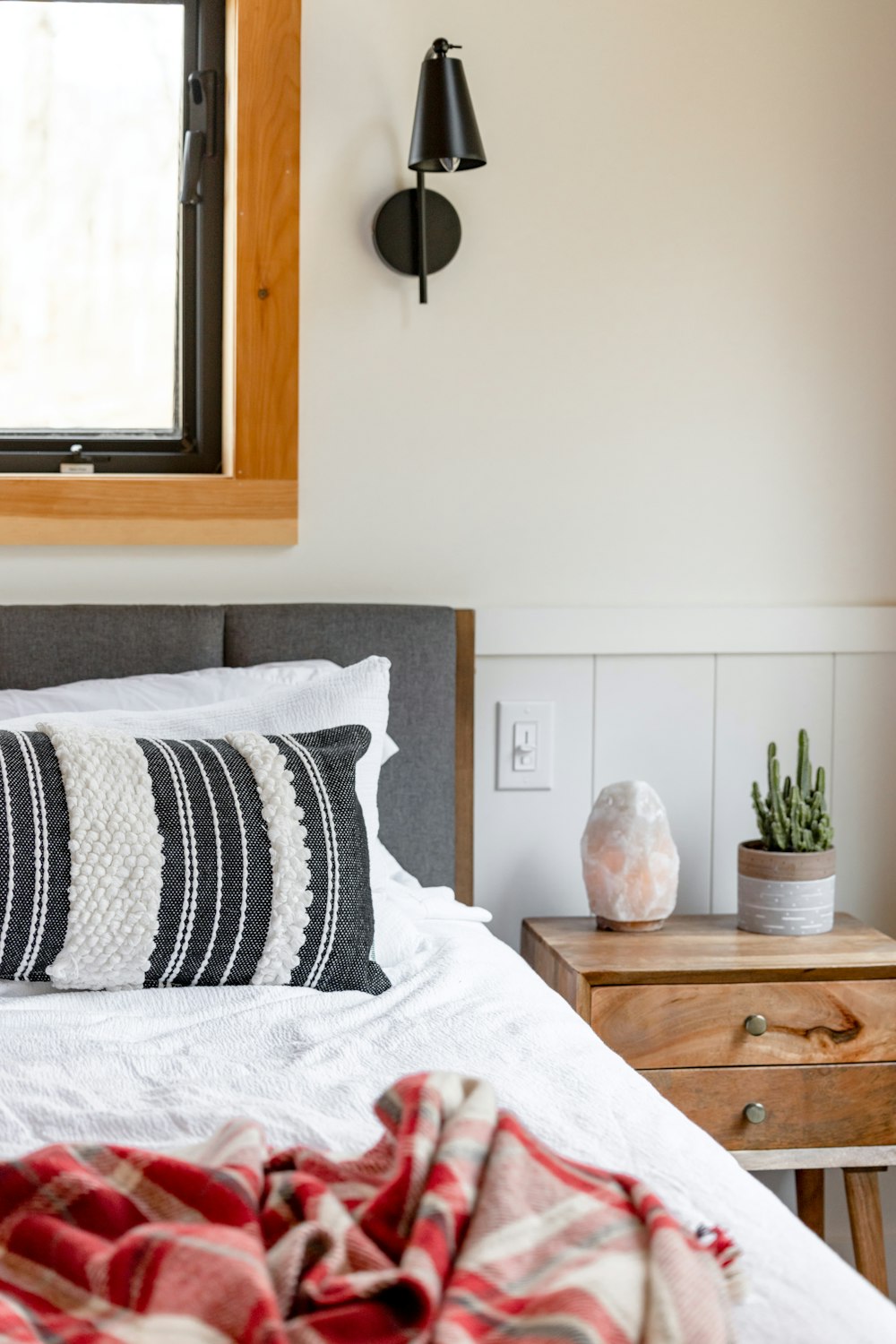 a bed with a red and white blanket and a lamp on the wall