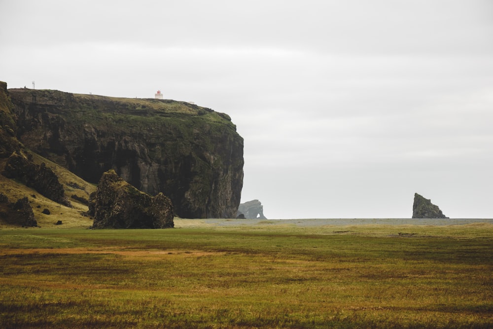 a grassy field with a rock formation in the distance