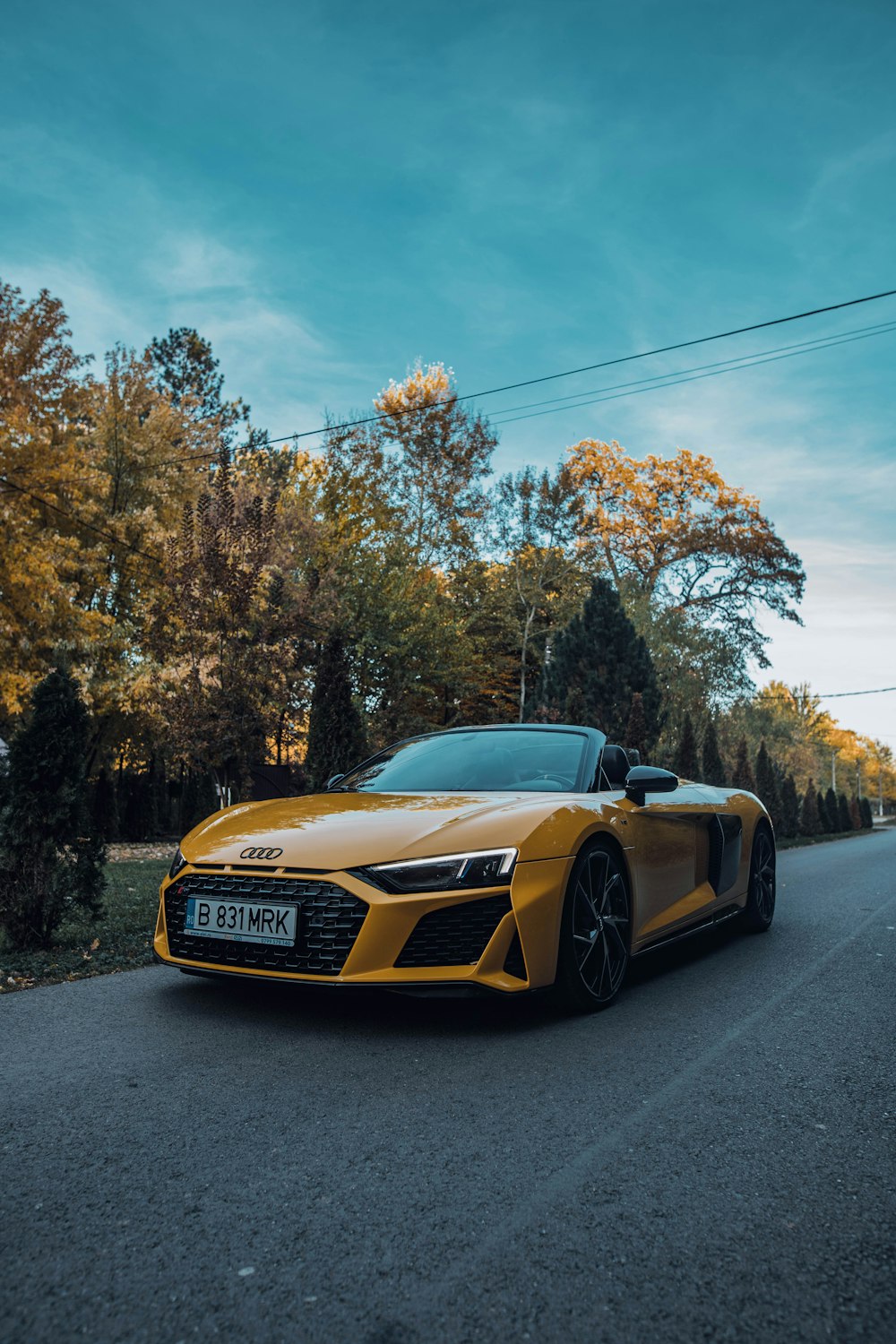 a yellow sports car parked on a road with trees on the side