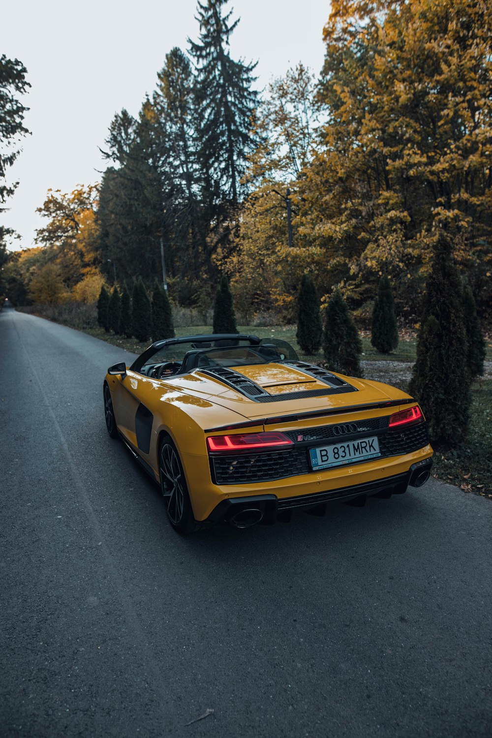 a yellow sports car on a road with trees on either side