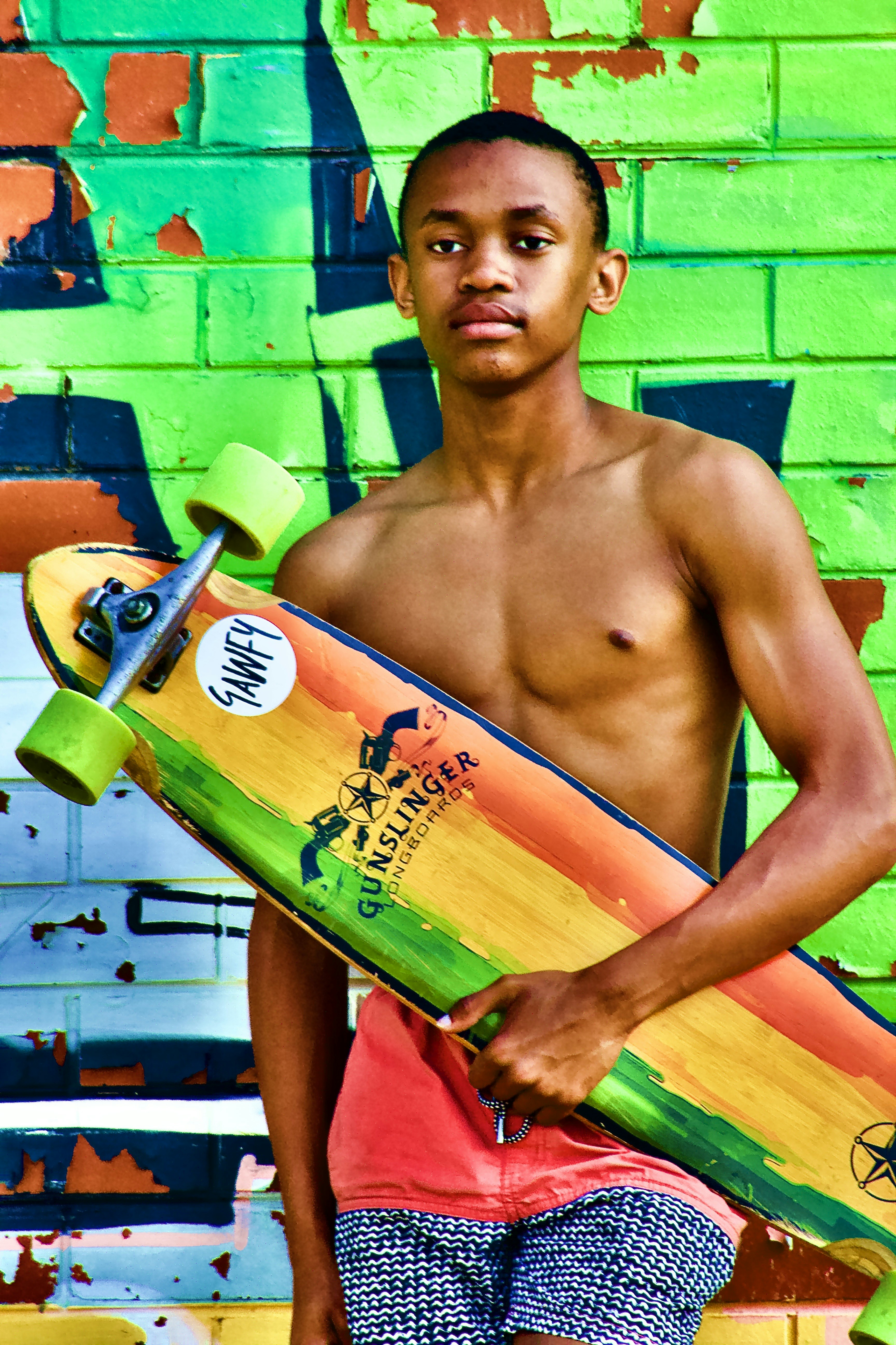 Young man holding a colorful skateboard against graffiti wall