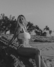 A charming Russian woman in a white bikini smiling softly against a beach backdrop.