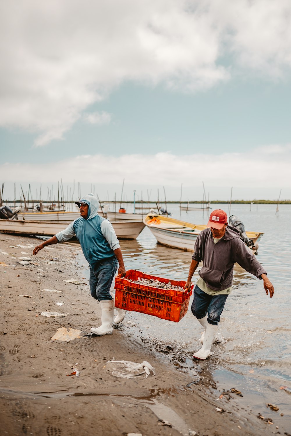 a couple of men in a muddy area with boats in the background