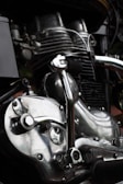 Close-up view of a motorcycle engine showcasing intricate mechanical parts. The metal components are highly polished, reflecting light with a shiny, silver appearance. Various pipes and bolts add to the complexity and industrial aesthetic.