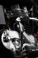 Close-up view of a motorcycle engine showcasing intricate mechanical parts. The metal components are highly polished, reflecting light with a shiny, silver appearance. Various pipes and bolts add to the complexity and industrial aesthetic.