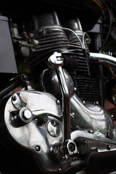 Close-up view of a motorcycle engine showcasing intricate mechanical parts. The metal components are highly polished, reflecting light with a shiny, silver appearance. Various pipes and bolts add to the complexity and industrial aesthetic.