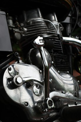 Close-up view of a motorcycle engine showcasing intricate mechanical parts. The metal components are highly polished, reflecting light with a shiny, silver appearance. Various pipes and bolts add to the complexity and industrial aesthetic.