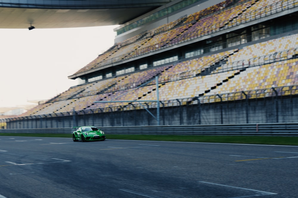 a green race car driving on a track next to a large stadium