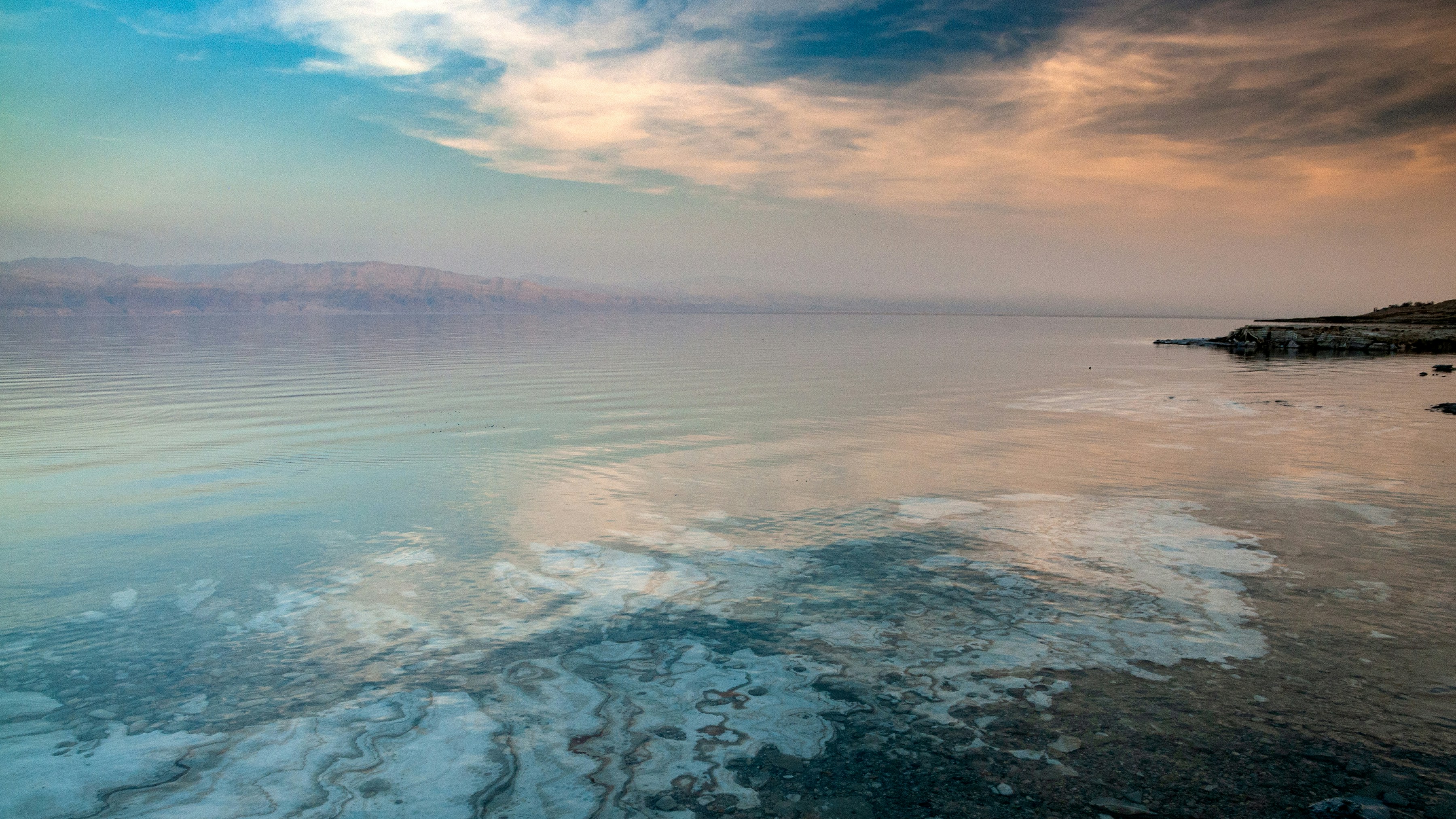 a body of water with a beach and mountains in the background