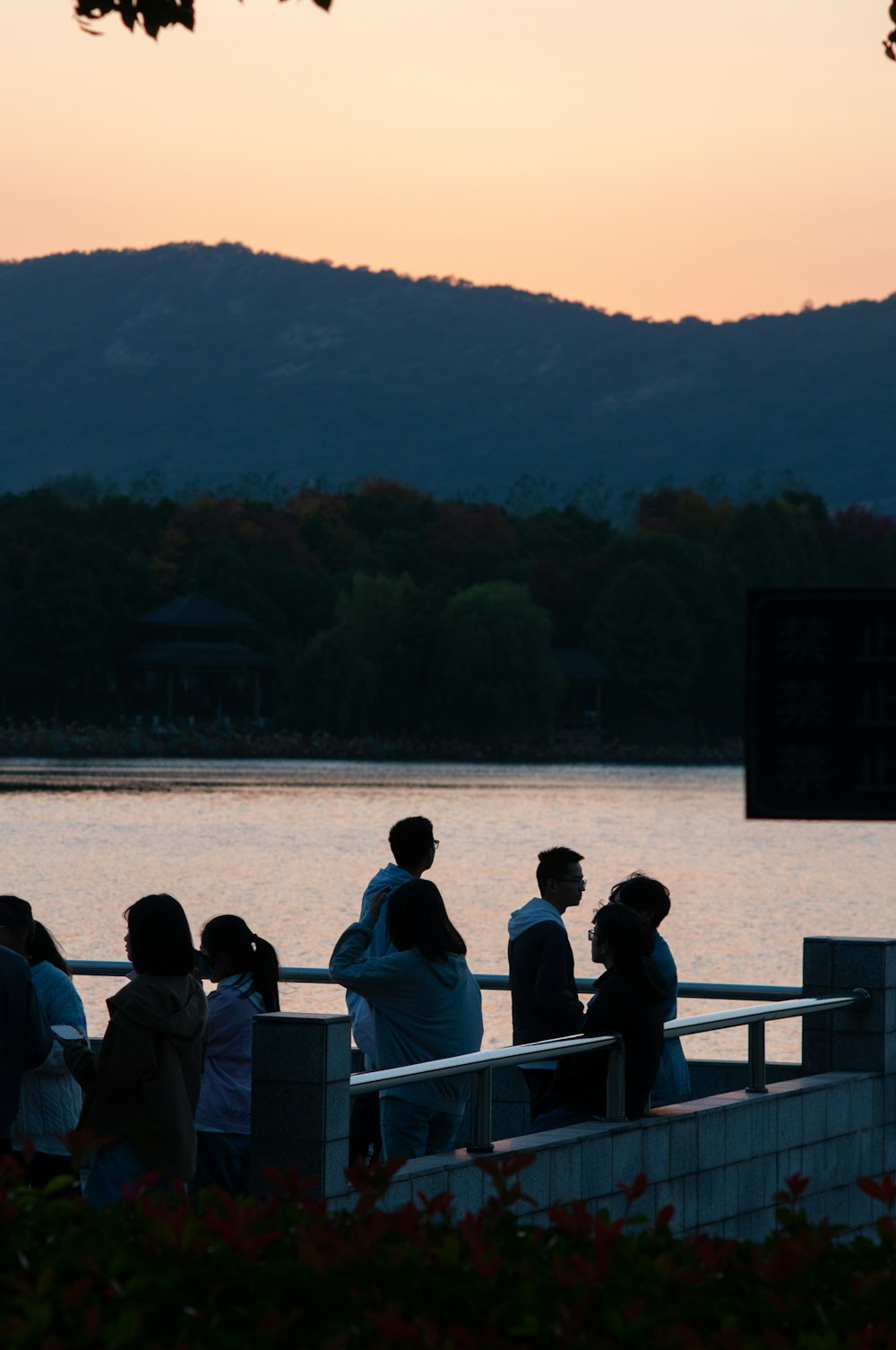 a group of people sitting on a railing overlooking a lake