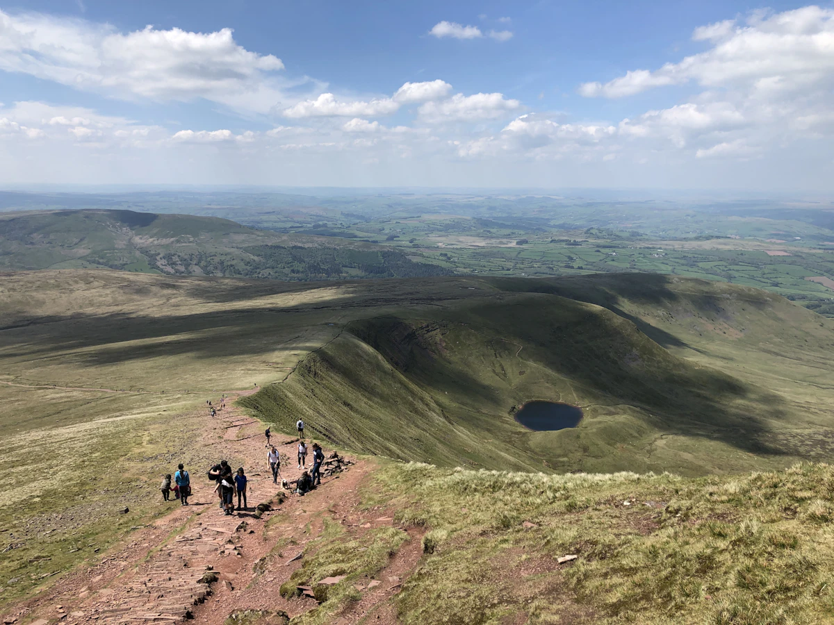 Walkers on a stony path along a Pen y Fan ridge above a small round lake