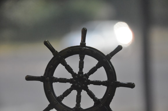 Black and white photograph of a vintage ship's wheel overlooking the sea horizon symbolizing navigation.