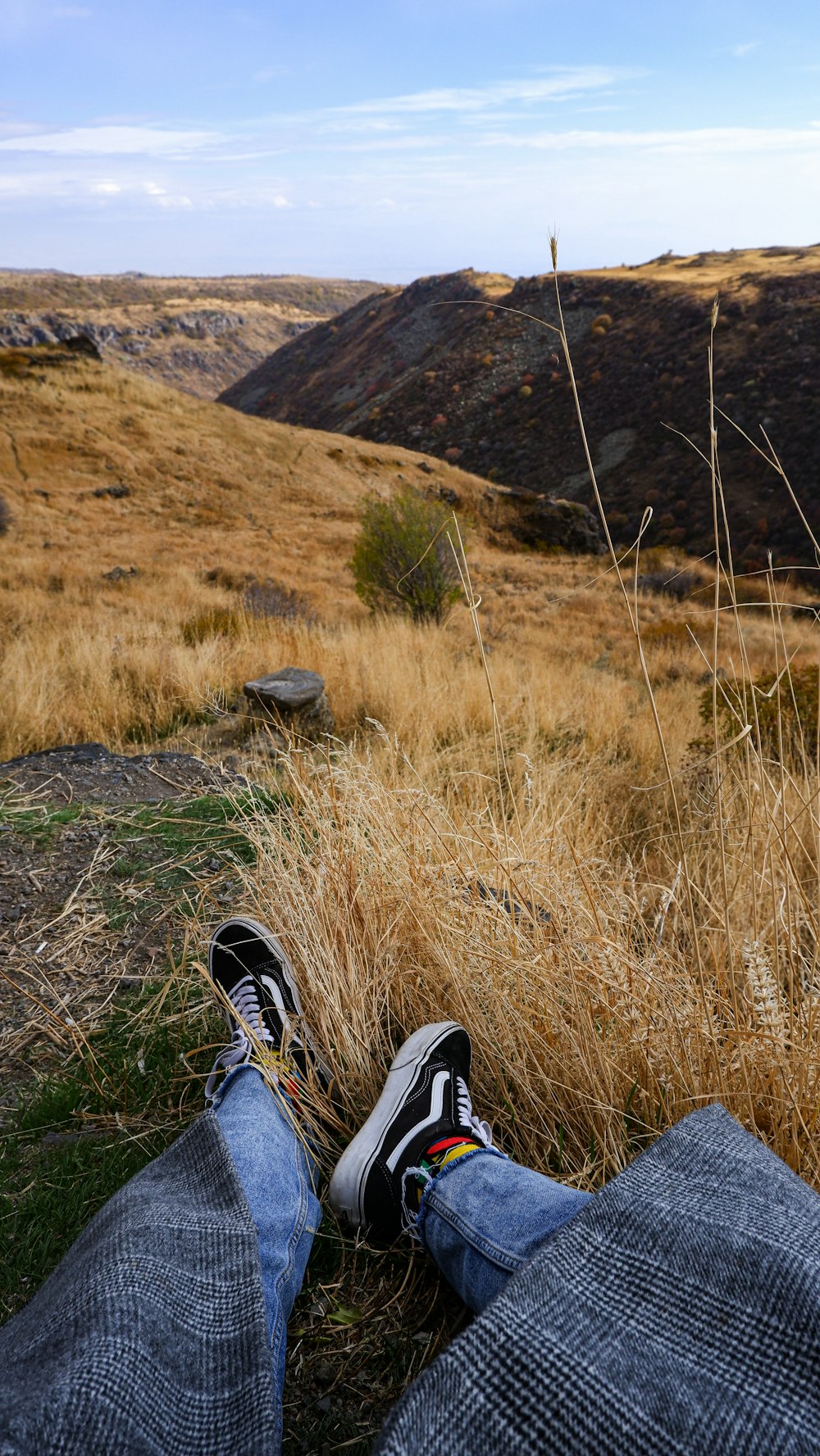 a person's legs and feet on a rock ledge overlooking a valley