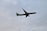 A commercial airplane is flying at a low altitude against a cloudy sky. The aircraft has a green tail and logo, while the rest of its body is predominantly white.