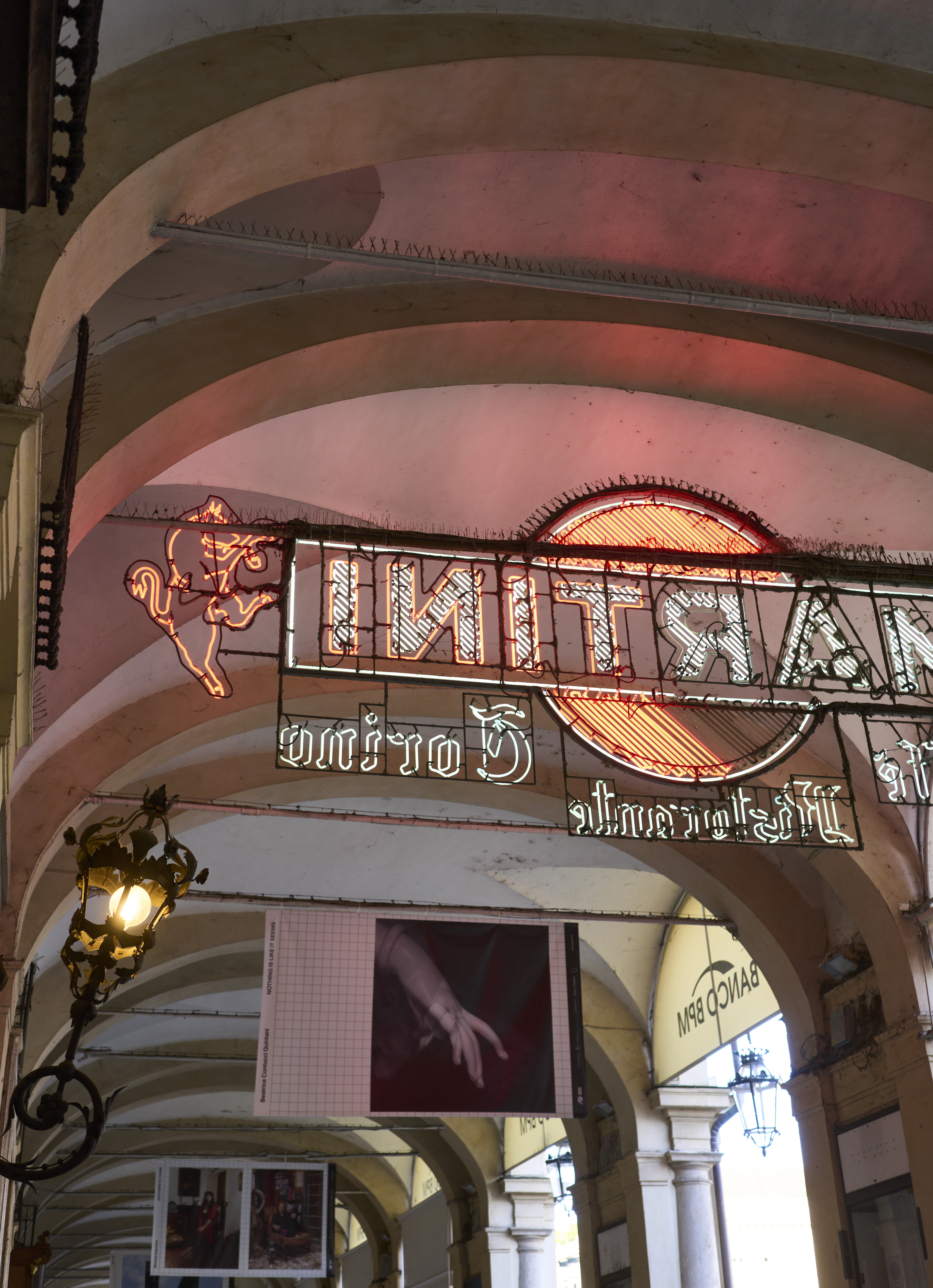 A vintage illuminated Martini sign glows beneath the stone arches of Turin's porticoed streets.