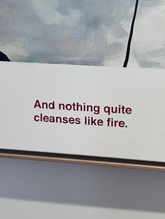 A canvas with text reading 'And nothing quite cleanses like fire.' in red letters. The background features an abstract blend of muted colors including shades of white, gray, and a hint of blue with a vertical black line cutting through the upper right corner.