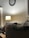 A cozy room with a lighted lamp on a small table near a wall adorned with a clock. A dog is comfortably nestled on a couch, partially covered by a plaid blanket.