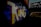 Large, colorful graffiti art spelling 'KING' in bold letters on a brick wall, set in a dimly lit underpass or tunnel with a nearby bridge structure visible in silhouette.