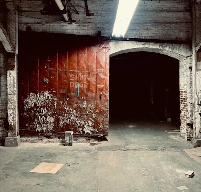 A rustic warehouse door opening to reveal open storage space under a cloudy sky.