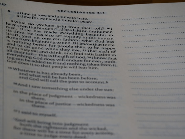 A close-up view of an open book showing text from Ecclesiastes 4:1. The text is typed in a serif font, and the page features numbered verses with a visible heading. The content discusses the human condition and philosophical reflections. The lighting is soft, casting slight shadows.