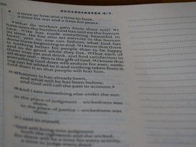 A close-up view of an open book showing text from Ecclesiastes 4:1. The text is typed in a serif font, and the page features numbered verses with a visible heading. The content discusses the human condition and philosophical reflections. The lighting is soft, casting slight shadows.