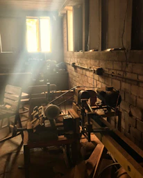 A sunlit workshop filled with wooden planks, tools, and a half-finished custom cabinet.