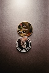 Two Ethereum coins, one gold and one silver, are placed on a textured surface. The coins feature the Ethereum logo and inscriptions related to decentralized platforms and smart contracts.