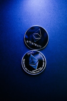 Two Ethereum coins with a metallic surface lie against a dark blue background. The top coin displays the Ethereum logo and text, while the bottom coin highlights the phrases 'decentralized platform' and 'smart contracts'.