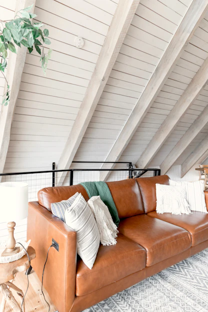 A warm, inviting living room featuring a fabric sofa bed with rustic wooden accents, a glowing lantern on a side table, and a knitted throw pillow adding texture.