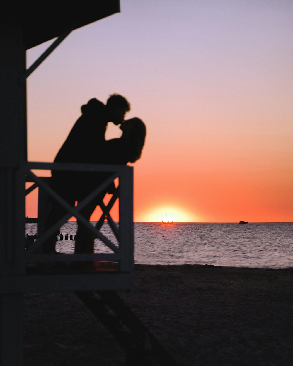 a silhouette of a couple of people sitting on a bench looking at the sunset