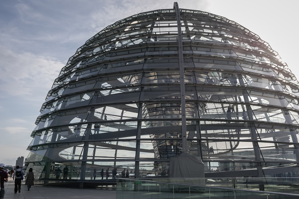 un grande edificio di vetro con persone che camminano con la cupola del Reichstag sullo sfondo