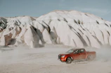A drive-away truck cruising along a desert highway with red rock formations in the background.