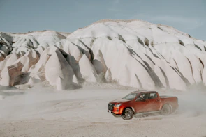 A drive-away truck cruising along a desert highway with red rock formations in the background.