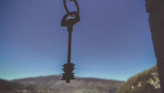 Hands exchanging keys with a backdrop of houses and blue sky.