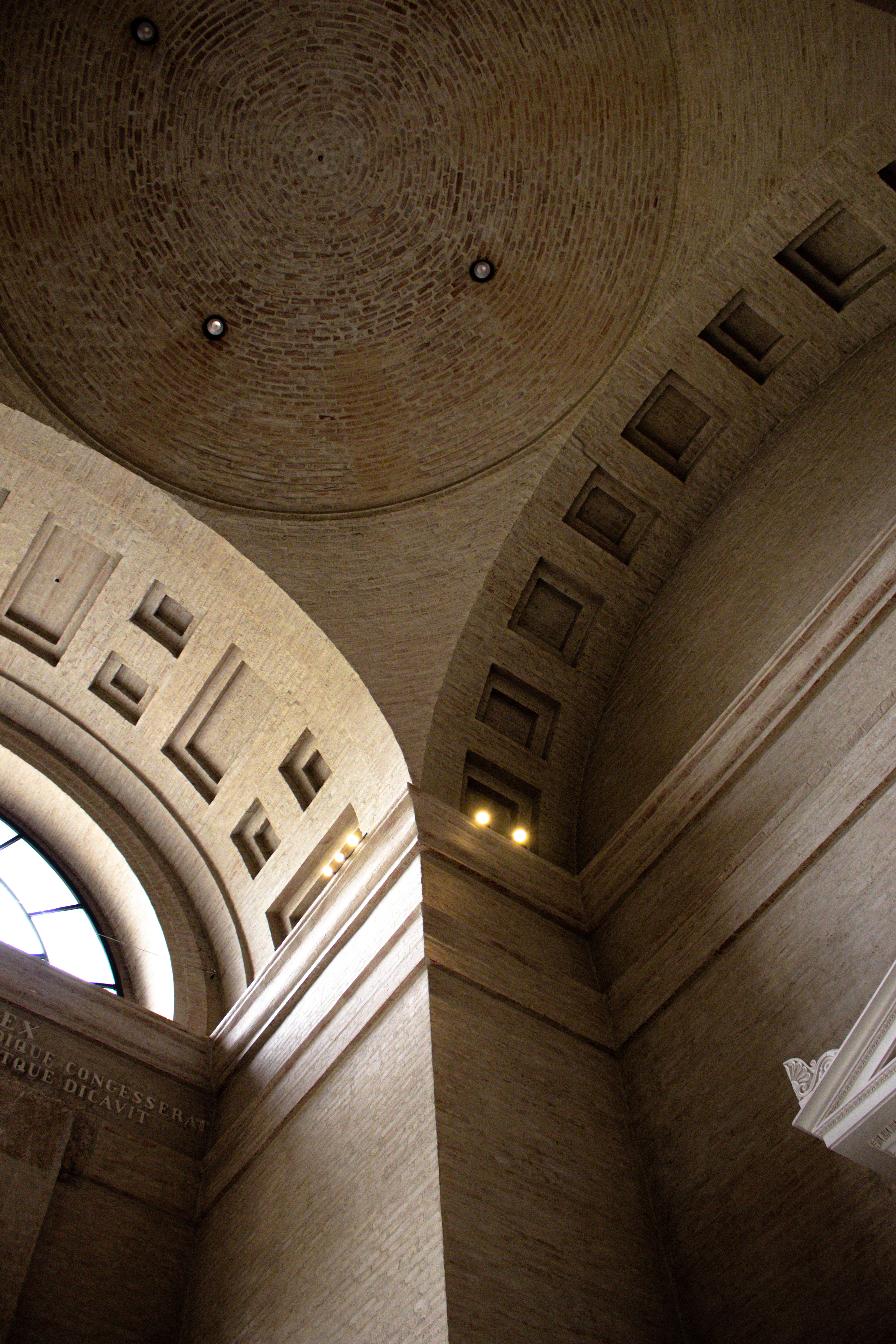 Coffered stone vault and arched window seen from below, lit by small recessed lights