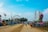 A vibrant amusement park scene with various rides including a large Ferris wheel and a colorful, rocket-shaped ride. The sky is clear and blue, creating a cheerful atmosphere. People are seen walking along a paved pathway, enjoying the attractions and atmosphere.