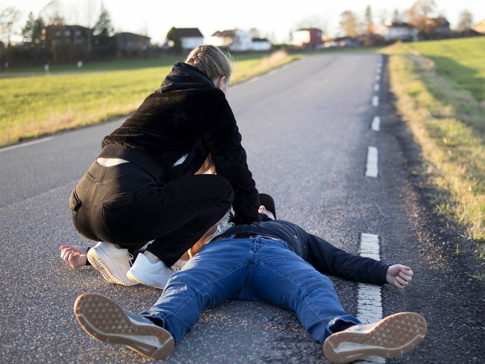 a man kneeling on the side of a road with another man kneeling on the ground