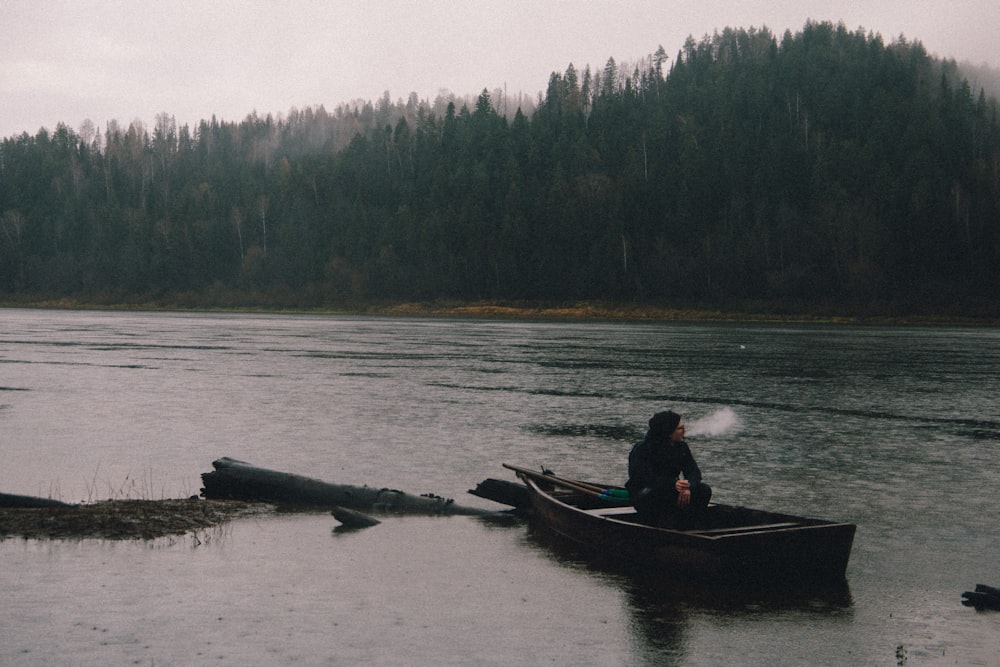 a man in a boat on a lake with trees in the background