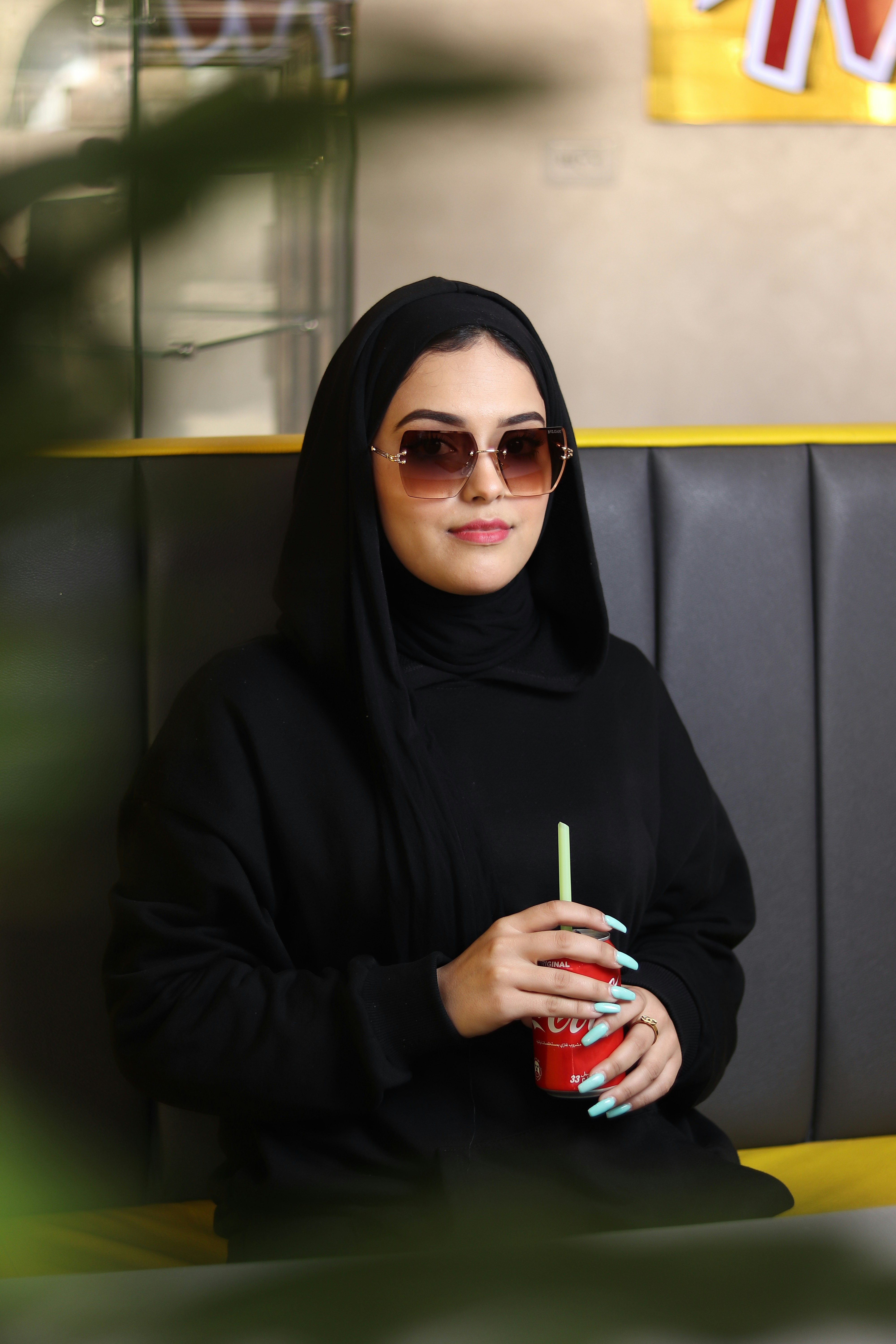 Seorang wanita mengenakan jilbab hitam dan memegang minuman