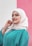 A person wearing a cream-colored hijab and a teal garment is smiling gently while looking at the camera. The background consists of two vertical color blocks in white and pink. The person exhibits a calm and confident demeanor, accessorized with a bracelet.