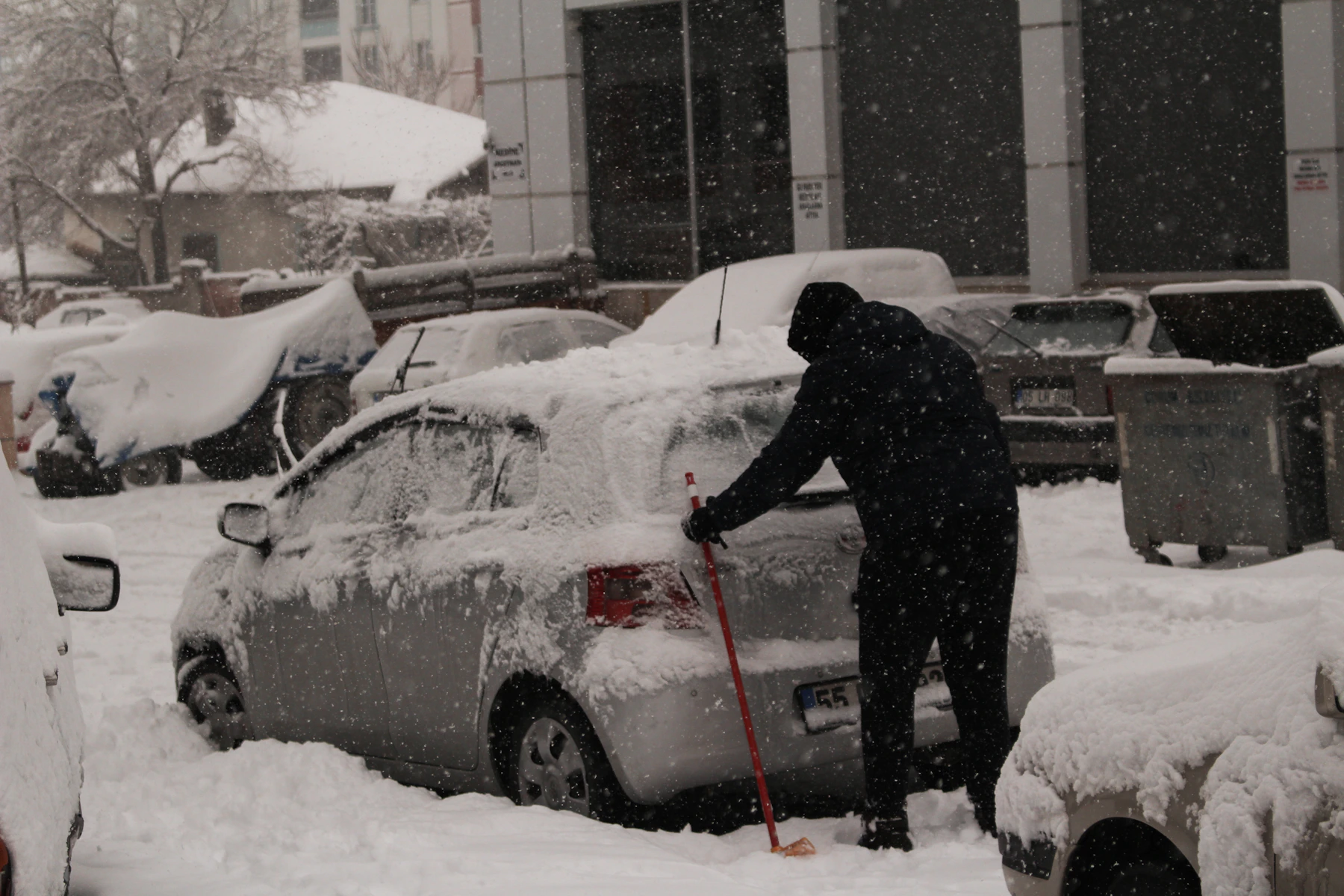 Person befreit ein verschneites Auto vom Schnee
