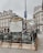 An ornate entrance to a metro station in a Parisian street, featuring decorative railings and a map of the metro network. Surrounding the entrance are historical buildings with classic French architecture. The atmosphere is overcast, and people are seen in the background.