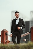 A groom confidently wearing a sleek black tuxedo with gold accents in a softly lit studio.