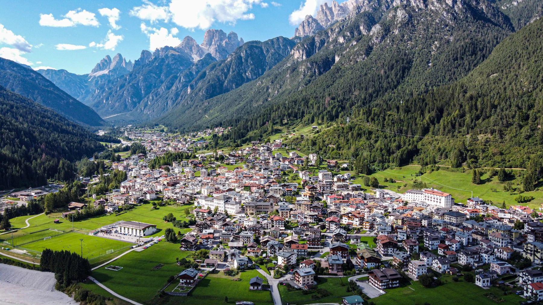 Photograph of Cortina d'Ampezzo spreads across a green valley beneath high limestone mountains.