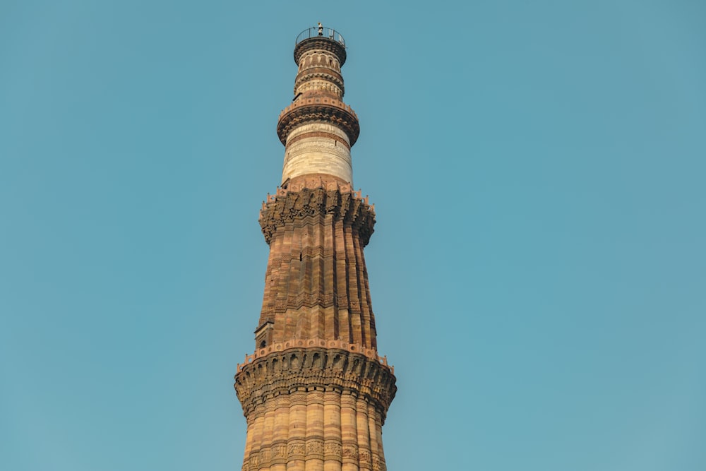 a tall tower with a circular top with Qutub Minar in the background