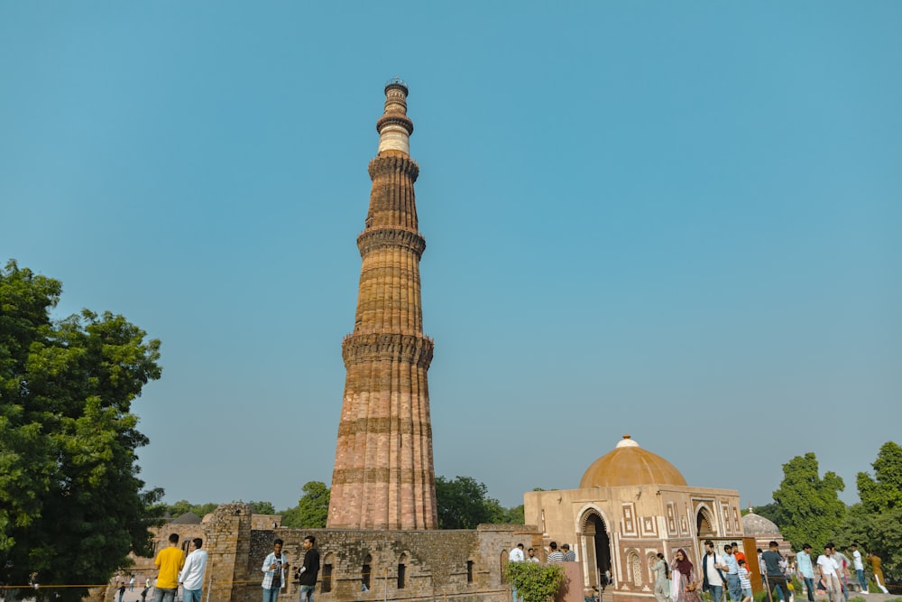 a tall tower with people around it with Qutub Minar in the background