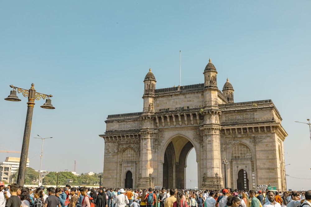 a large group of people outside a large stone building with Gateway of India in the background