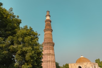 a tall tower with trees around it with Qutub Minar in the background