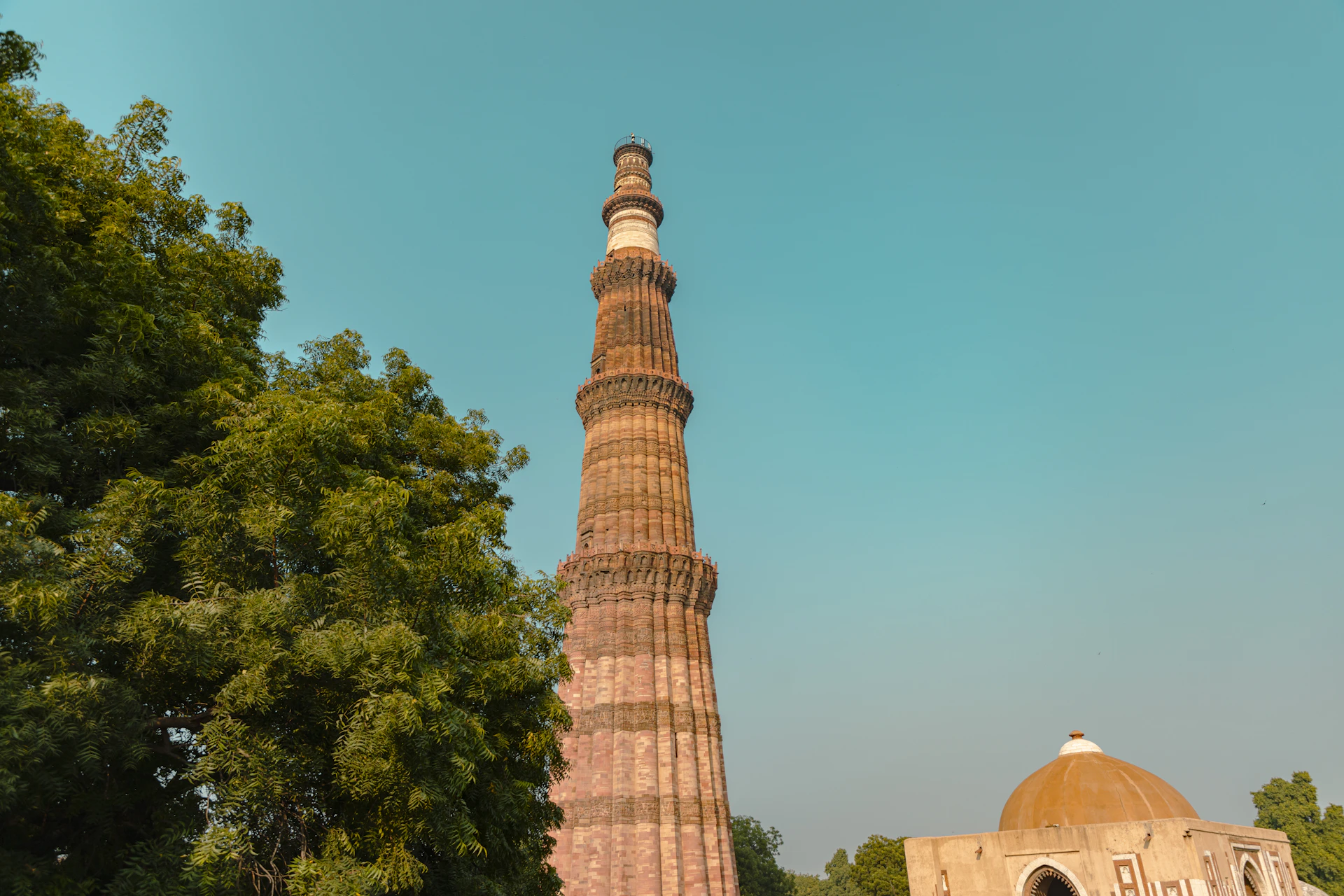 a tall tower with trees around it with Qutub Minar in the background