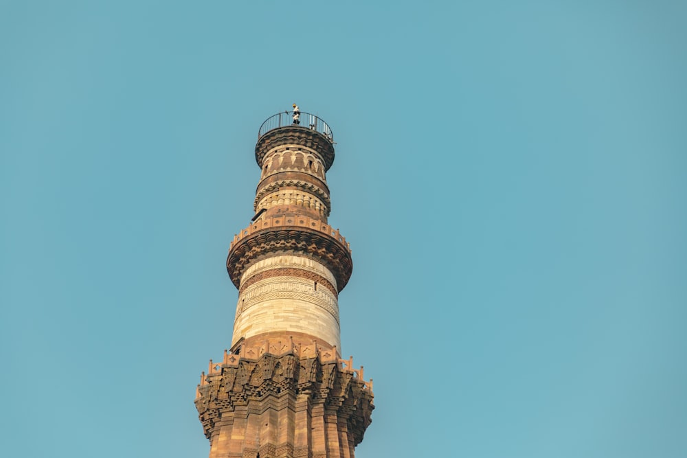 a tall tower with a circular top with Qutub Minar in the background